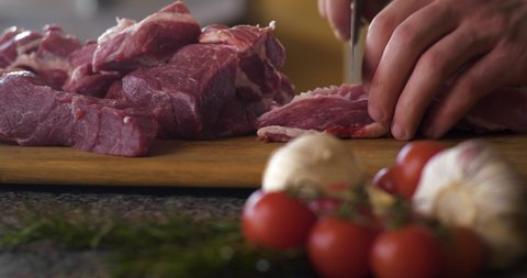 Beef fillet on the Cut Board, preparing Meat. Brutal Mans`s Hands with a Knife slicing, cutting a delicate Beef fillet Meat on the cut board. Beef or Veal meat on the Table. Steak. Meat Dish.