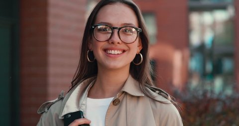 Young Attractive Woman posing on Camera while standing on the central Square. Having stylish Eyeglasses and Earrings. Looking gorgeous and having nice Appearance. Wearing trendy Trench.