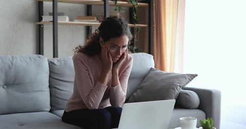 Serious young woman in eyewear working remotely on computer, feeling stressed about information or electronic report loss. Depressed unhappy female distant worker received email with dismissal notice.