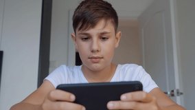 Close-up portrait of boy playing mobile game on smartphone at home. Preschooler playing mobile phone. Kid using phone for gaming. Child playing video game.