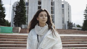 A slow motion close up video of a young woman in white clothes taking a walk in the park and being filmed by the camera from the front