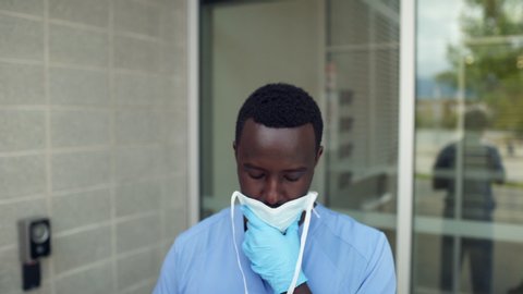 African American black man nurse doctor wearing PPE adjusting blue medical mask, walks out of frame, medium frame. 4K.