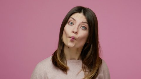 Closeup funny young woman showing fish face, duck grimace with pout lips, looking amazed stupid, making humorous dumb expression, sucking and choking. indoor studio shot isolated on pink background