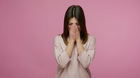Lovely happy brunette young woman looking at camera with regret sadness, crying hard and hiding face with tears in hands, desperate emotions, depression. indoor studio shot isolated on pink background