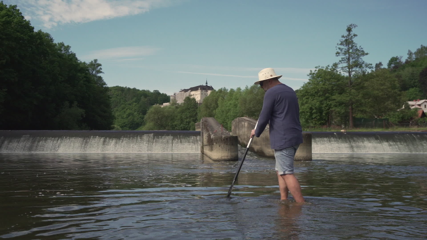 Male paddler checking water level of Sazava river with paddle, weir in background
