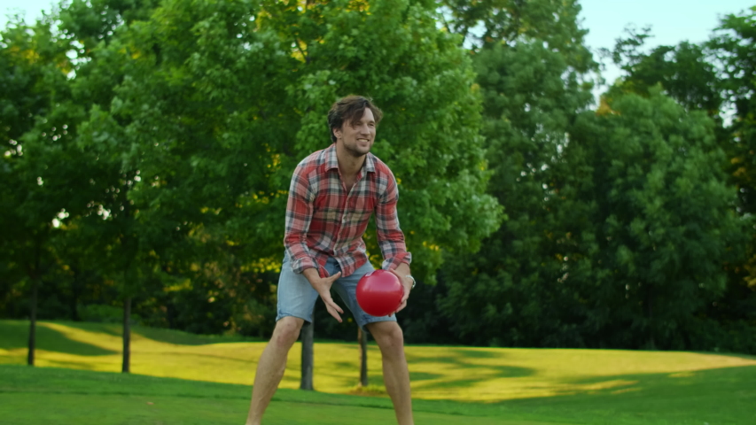 Active family enjoying summer outdoor activity together. Happy parents and kids playing with ball in meadow. Positive father throwing ball in air. Pretty girl catching ball in green field