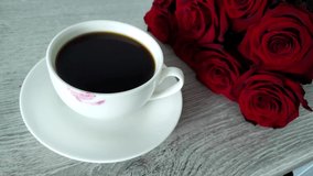 video with a cup of coffee and female lipstick left on it and a bouquet of red roses in the background