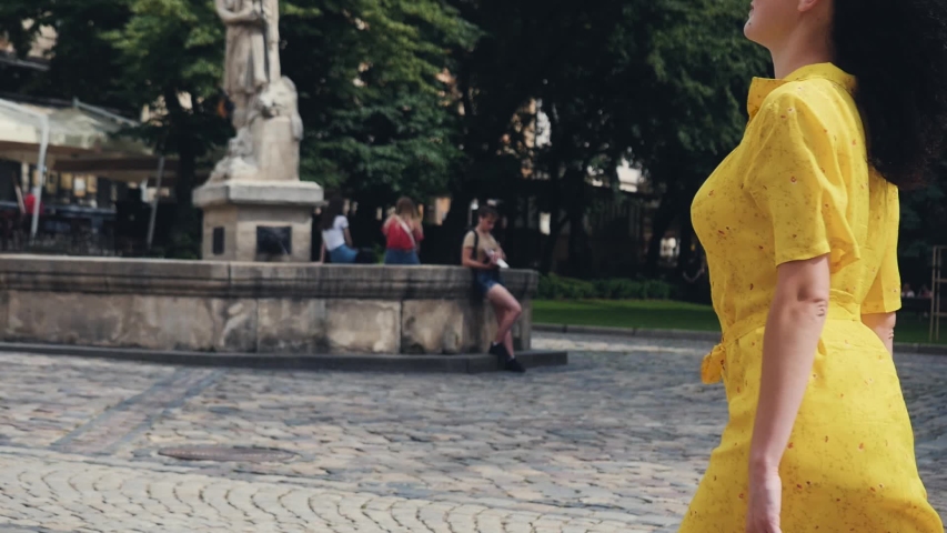 Beautiful young woman curly hair yellow dress red handbag walking urban city background. Gorgeous Happy smile cute fashion young woman. Urban, street, lifestyle concept. Back view