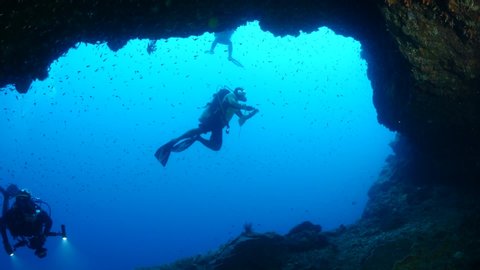 scuba divers exploring underwater cave scenery with corals and tropical fish healthy ocean scenery