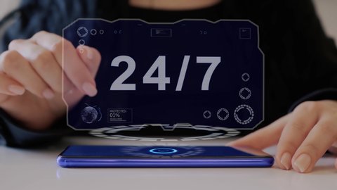 Female hand interacts HUD hologram with text 24 7. Woman in black uses conceptual holographic technology of the future on the screen of a smartphone lying on a table