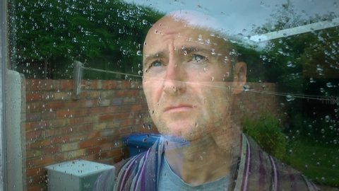 Mens mental health and well-being issues. A depressed, lonely male in self isolation, wearing a dressing gown. He from his house window. Coronavirus, covid-19 pandemic, depression ,male suicide.