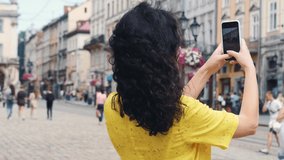Girl tourist weraing yellow dress photographing buildings architecture in Lviv city using camera and application on modern cellular phone, Female wanderlust