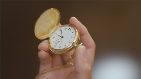 Woman's hand raises a pocket watch into frame and opens it before closing it back up