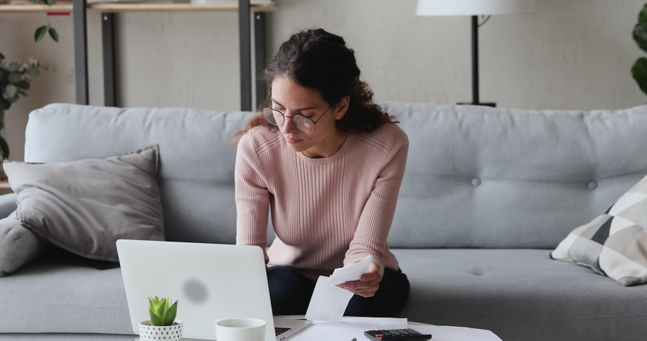Focused serious young woman in eyewear sitting at coffee table at home, managing personal monthly budget in computer application. Concentrated lady calculating incomes outcomes utility bills. Royalty-Free Stock Footage #1055020367