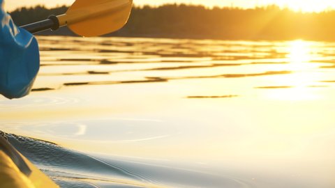 outdoor activities, a man rowing an oar in calm water on a kayak against a golden sunset, slow motion