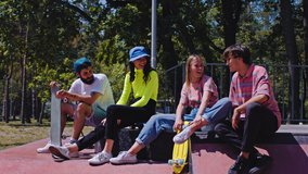 In a good sunny day group of friends very attractive multiethnic enjoying the time in a modern skate park they sitting on the floor and socializing before start to skateboarding. 4k