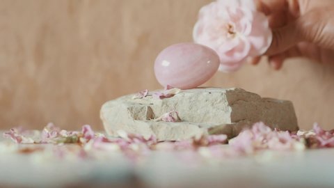 Female hand take Yoni rose quartz egg in rose petals on a background of natural flesh-colored clay similar to human skin
A sacred instrument for intimate practices of female health and sensitization