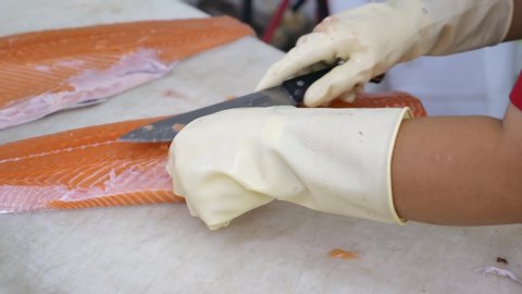 Close-up of Worker Hands Cutting and Cleaning Salmon Fillet by Big Chopping Knife in Grocery Store. Fresh Fish Clean and Cut Process in Supermarket