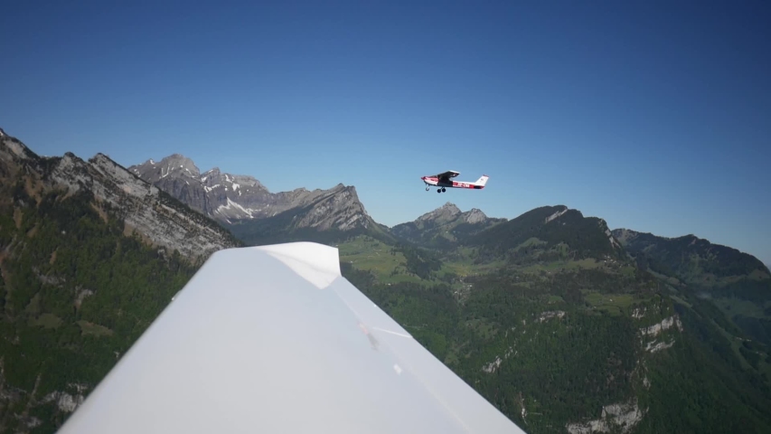 Formation flight with view from inside a small private plane over the wing. Swiss mountain peaks in the background, beautiful, panoramic and green scenery. Aerial shot over Switzerland.