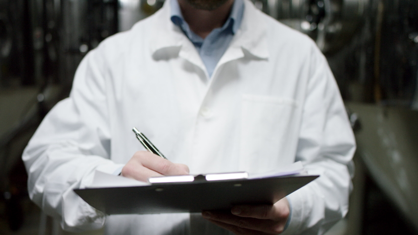 A mature factory male worker is making a list of all requirements for a product. A front view slow motion close up