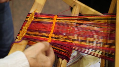 Close-up of womans hands weaving with traditional weaving machine. Home weaving machine. Detail of traditional vintage weaving hand loom with wool close up. Traditional old loom