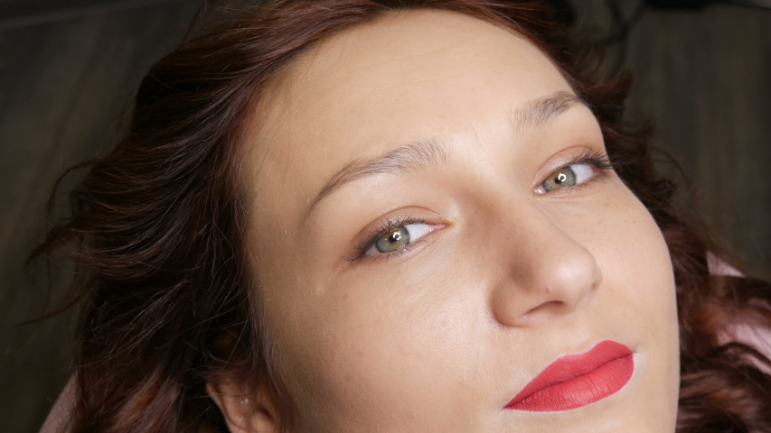 Portrait of a beautiful young woman before permanent makeup by microblading with eyebrow tattoo and lips with red lipstick lies on a couch in a beauty salon..