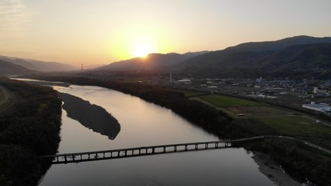 4K Aerial Drone Footage of Waki Town Submersible Bridge on Yoshino River at Sunset with Beautiful Sunset Sky. One of the West Awa View Point 100 Selections in Tokushima Prefecture.