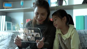 A futuristic virtual simulation of an asian beautiful mother and a young daughter enjoy playing with an advance tablet mock up and answering an incoming video call at home
