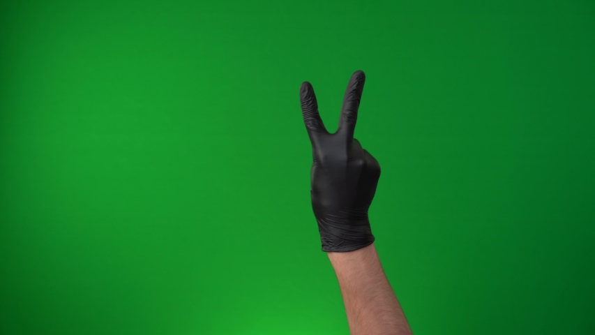 The V sign gesture, Victory or As an insult. Black Lives Matter. Hand in back medical glove isolated on a green background, chromakey. Covid-19