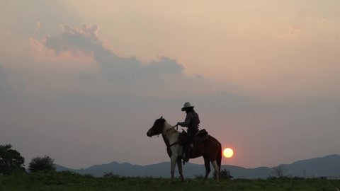 man in cowboy costume riding horse against sunset.