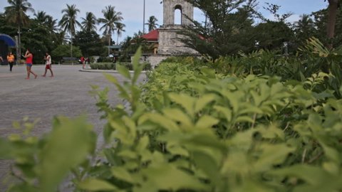 Landscape Of Green Plants And Trees Swaying On The Wind With Locals Visiting And Walking At The Magellan Shrine In Mactan Island, Cebu City, Philippines - panning up shot
