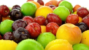 Fruit mix rotating on white background. Fresh organic macro red berry, green plum and yellow apricot fruit turning real shot 4K closeup background video  water drop.