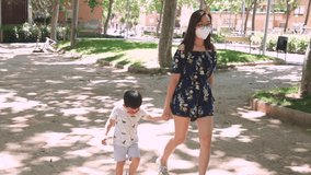 A woman and her son walking at an empty park wearing face surgical masks for protection against virus. New normality video outdoors. Coronavirus pandemic prevention measures