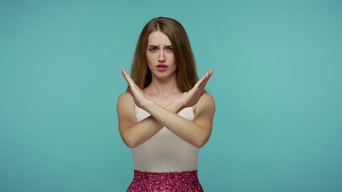 Displeased serious girl in dress crossed her arms in X sign and saying no, warning of finish, prohibited access, declining communication, body language. indoor studio shot isolated on blue background