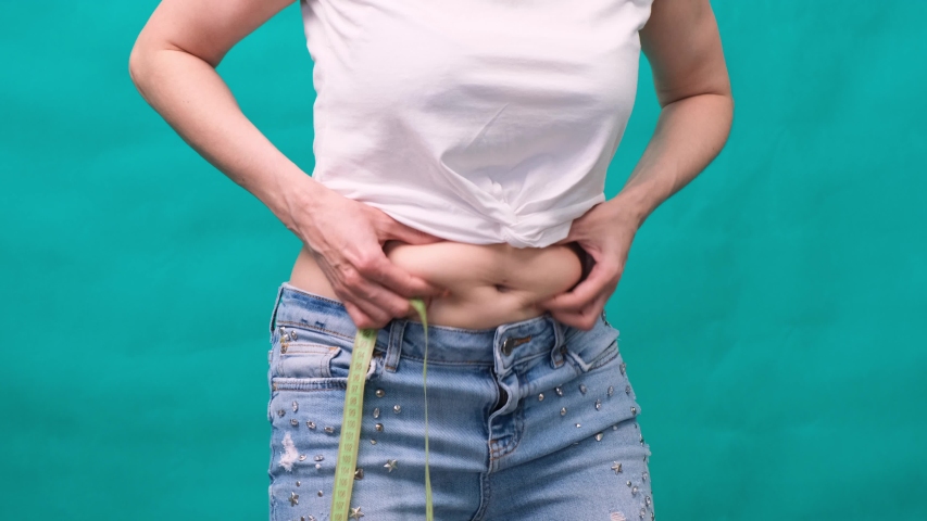 Woman holds a fold of skin on a thick belly, fat female body on a green background. Bold female waist. The concept of weight loss and diet Royalty-Free Stock Footage #1055046896