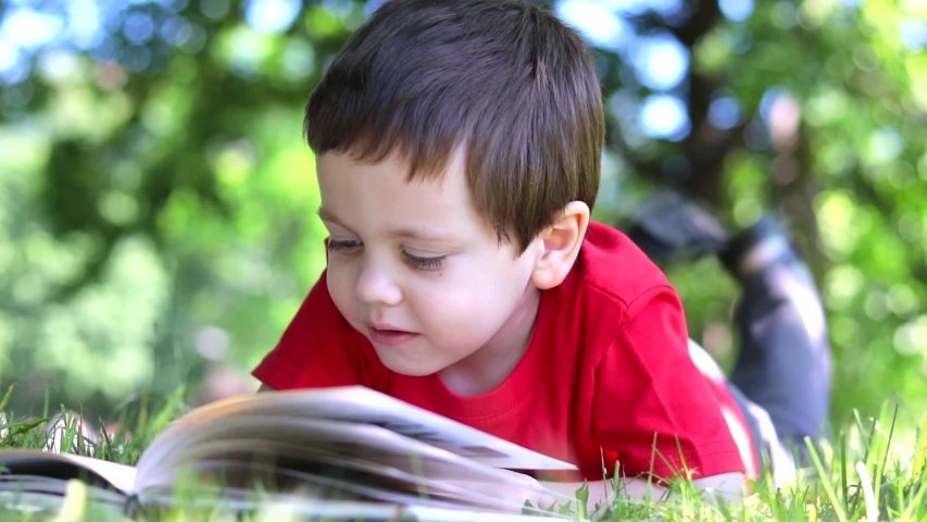 The boy is lying on the grass and reading a book . Extracurricular reading. Offline training. | Shutterstock HD Video #1055047610