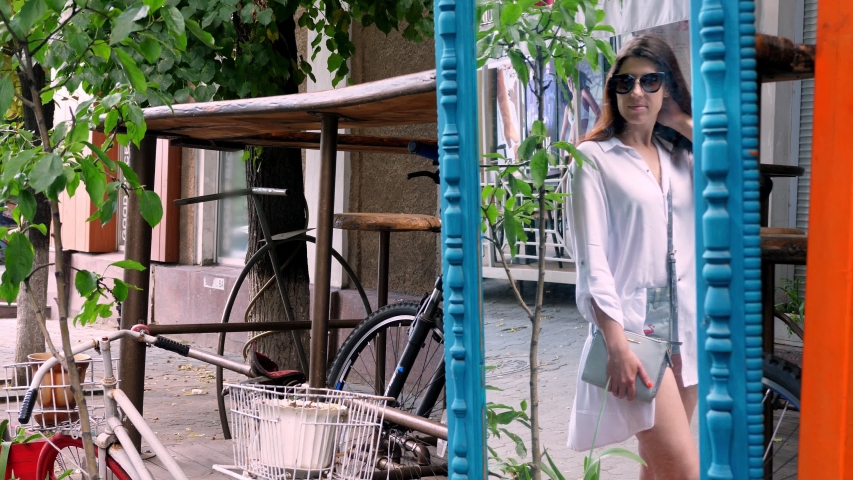 beautiful brunette woman, in sunglasses, admires herself in the mirror, outdoors, near the street vintage cafe. summer sunny day