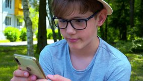 Portrait of a modern attractive teenage boy in glasses who is conducting a video blog using a smartphone on the street on a sunny summer day