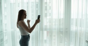 Young pretty woman have video call on the phone at home near window