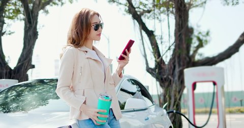 Kaohsiung,Taiwan - January 16, 2020 : asian woman use reusable eco-friendly ecological straw drink while using smart phone and waiting for charging the battery in Tesla electric vehicles