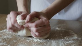 Female hands kneading dough in flour on the table, sunlight from the window illuminates the scene. Shallow depth of focus. Video taken close-up with natural light in 4k