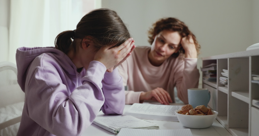 Unhappy young girl sitting at desk, suffering from pressure while doing homework with mother at home. Angry mom scolding stressed daughter for bad school results, parent and children conflict concept. Royalty-Free Stock Footage #1055062349