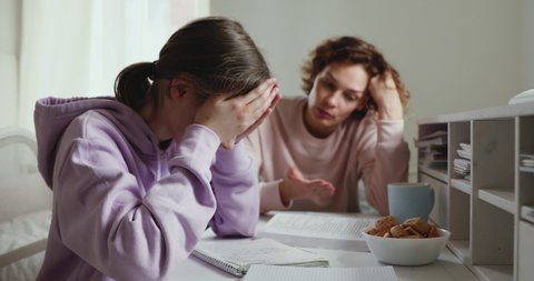 Unhappy young girl sitting at desk, suffering from pressure while doing homework with mother at home. Angry mom scolding stressed daughter for bad school results, parent and children conflict concept.