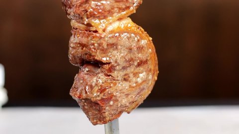 Waiter cuts a piece of meat from a barbecue skewer.