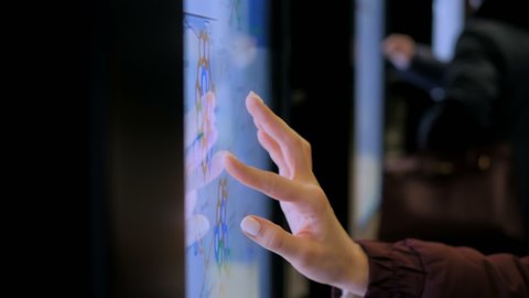Woman using modern interactive touchscreen display of electronic multimedia kiosk with city map at street - scrolling and touching. Navigation, journey and technology concept