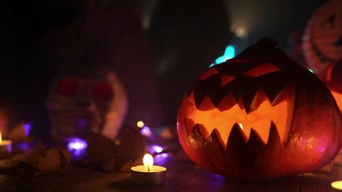 Jack-o-lantern is standing at wooden table with the burning flame inside. Close up loop video of the halloween symbol standing in front of other decorations. Theme of halloween and it's symbols.