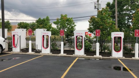 Staten Island, New York / United States - June 21 2020: Tesla electric car charging station set up in strip mall parking lot. Wide shot, slow pan of charging units empty parking spaces.