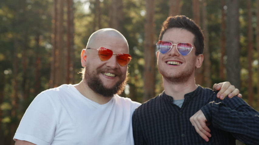 Homosexual couple dating in nature. Portrait of two affectionate gay men in love wearing sunglasses showing paper heart and smiling to camera. LGBTQI, Pride Event, LGBT Pride Month, valentine's day Royalty-Free Stock Footage #1055069918