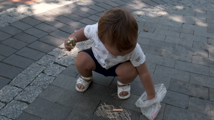 Cute little girl draws with chalk on the sidewalk.