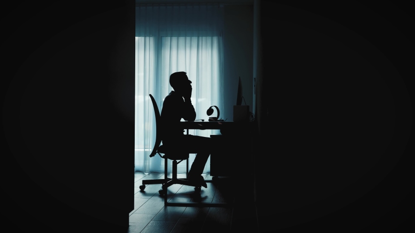 Silhouette shadow of a man at the computer in short time work at home office plagued by existential fears and anger about the situation. Keywords are shown. Depression, isolation, crisis, burnout. Royalty-Free Stock Footage #1055071088